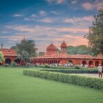 A scenic view of the Red Fort gardens in Delhi, showcasing its historic architecture and lush greenery at sunset.